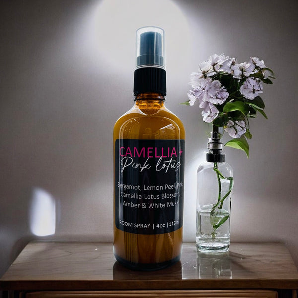 Camellia Pink Lotus room spray bottle on a wooden surface with a small vase of flowers.