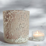 A large cylindrical marble-patterned pink and white glass candle jar with a lit tea light candle beside, placed on a marble surface.