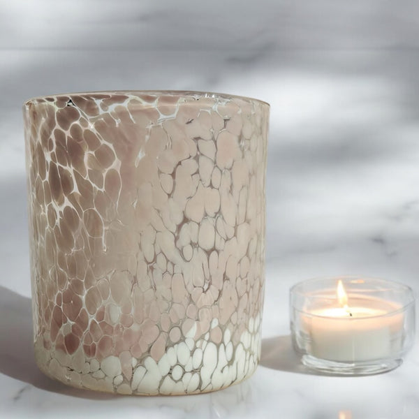 A large cylindrical marble-patterned pink and white glass candle jar with a lit tea light candle beside, placed on a marble surface.