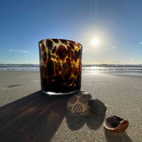 Large Vogue Leopard amber coloured glass candle jar on beach with sea behind and shells in front of jar